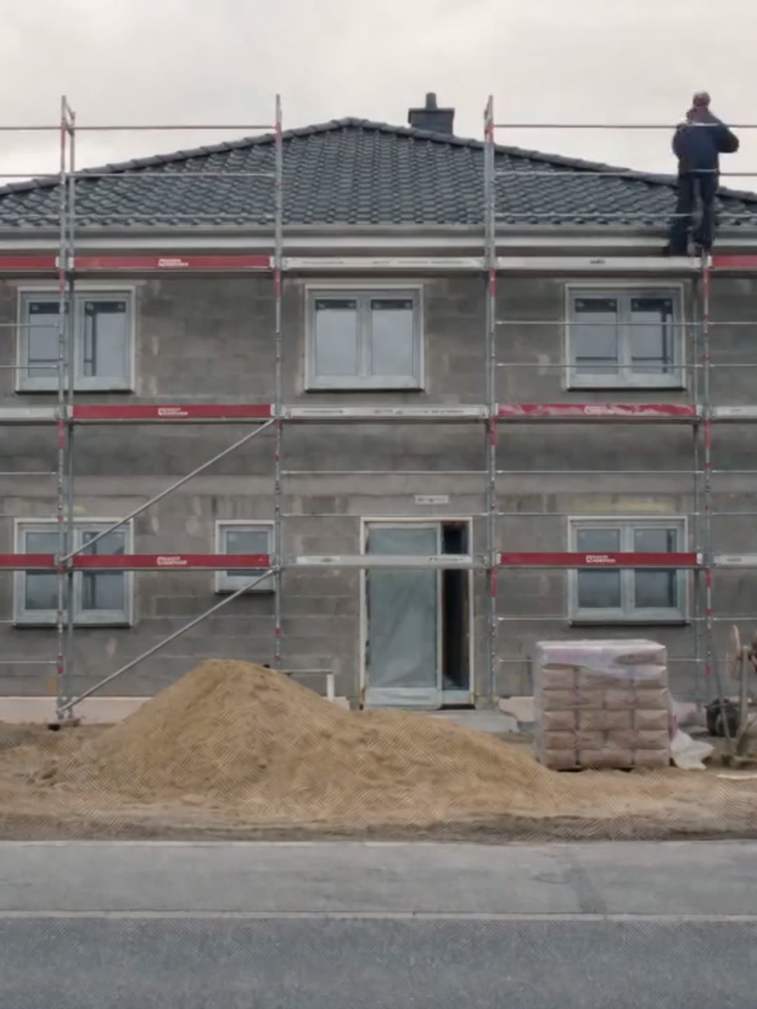 Eingerüstetes Wohnhaus im Rohbau, Handwerker auf dem oberen Gerüstboden
