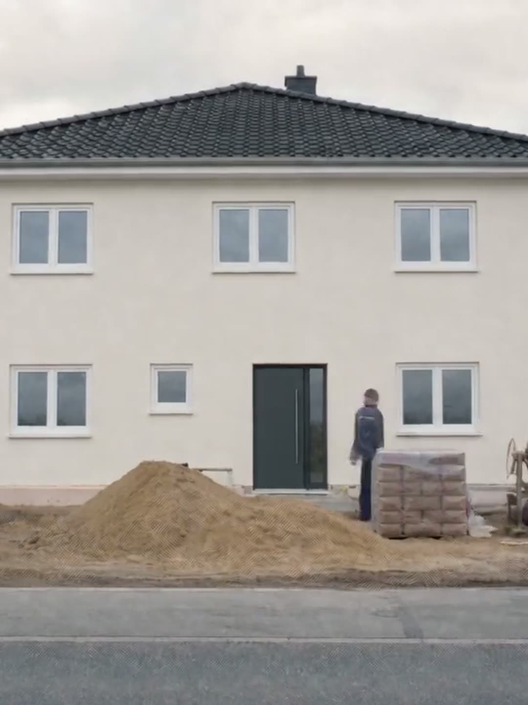 Weiß verputztes Haus, das Gerüst ist abgebaut, zwei Handwerker davor