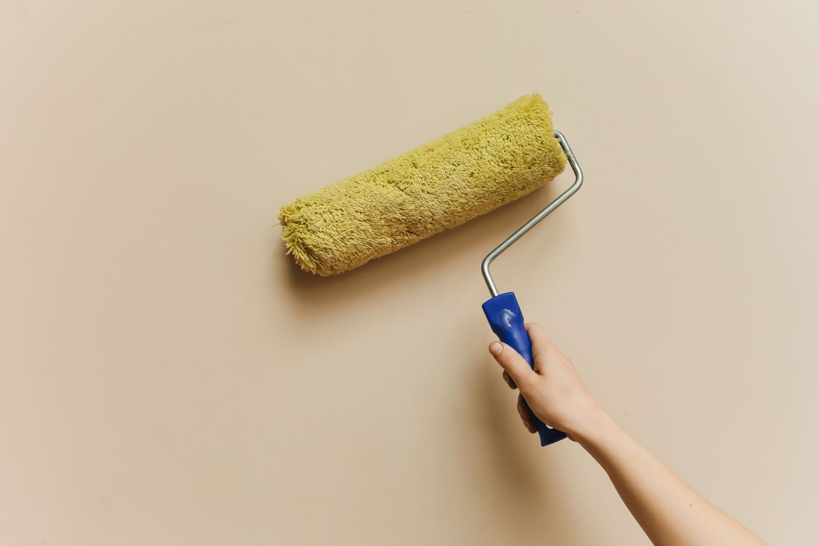 Farbroller trägt frische Wandfarbe auf eine beige Wand auf